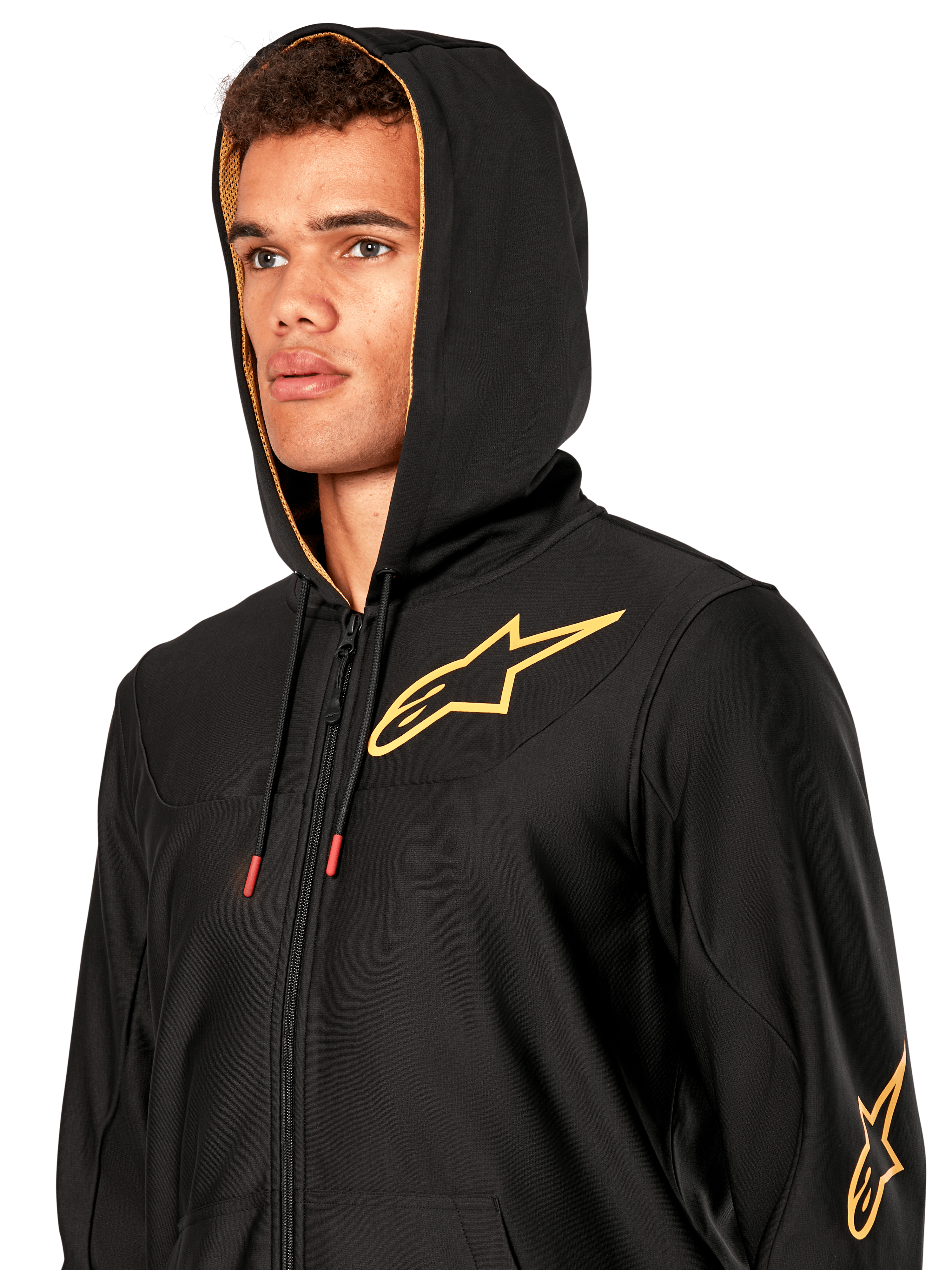 Man wearing Alpinestars Sessions V3 Hoodie, black zip-front fleece with gold star logo on chest, gold mesh-lined hood with tech drawcords, casual motorsport streetwear