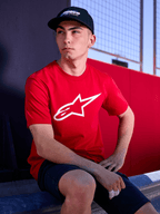 Alpinestars Profile Hat in Black, lifestyle shot of a man wearing the curved bill hat with a red t-shirt featuring a white Alpinestars logo, casual motorsport-inspired streetwear
