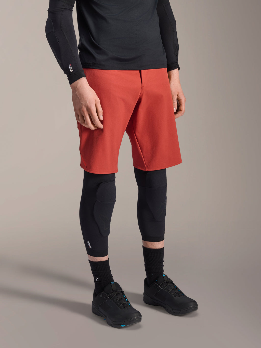 Alpinestars A-Motion Plasma Knee Sleeve, MTB Knee Protector, Black, worn with red shorts and black mountain bike shoes, low-profile slip-on design featuring contoured protective pads and breathable mesh.