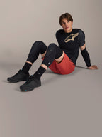 Alpinestars A-Motion Plasma Knee Sleeve, black mountain bike knee protectors, worn by a male model sitting in complete cycling gear with red shorts and black performance tee, showcasing the low-profile protective design.
