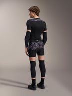 Model wearing Alpinestars A-Motion Plasma Protection Boxers in Black Camo and matching A-Motion Plasma Protection Jacket, rear view showing grey camouflage pattern, elbow guards, knee protectors, and cycling shoes, complete mountain bike protection gear setup.