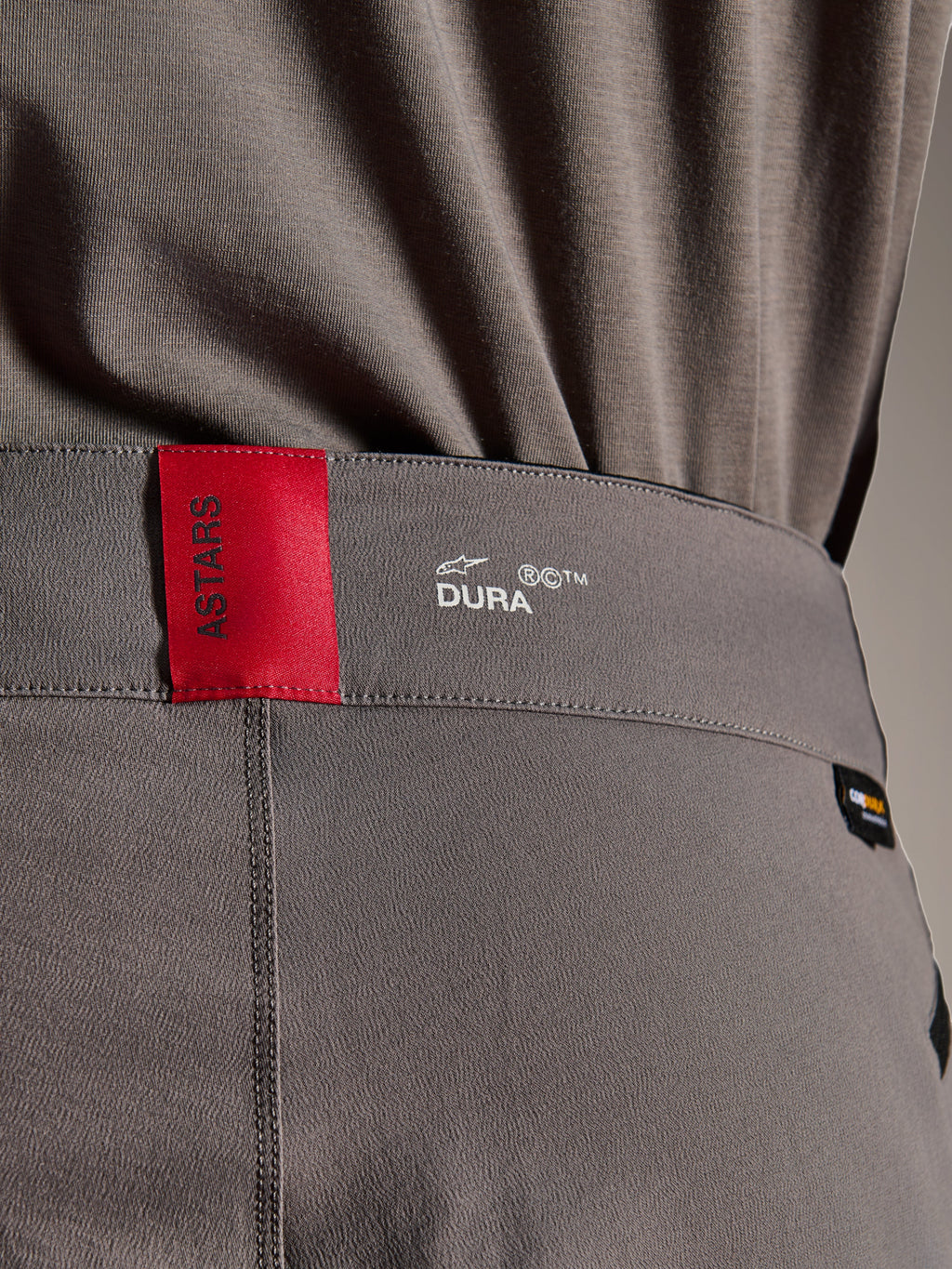 Alpinestars A-Dura Elite Pants, MTB Pants, Dark Gray, close-up of the waistband showing a red ASTARS tag and white DURA logo, featuring textured Cordura fabric and premium branding details.