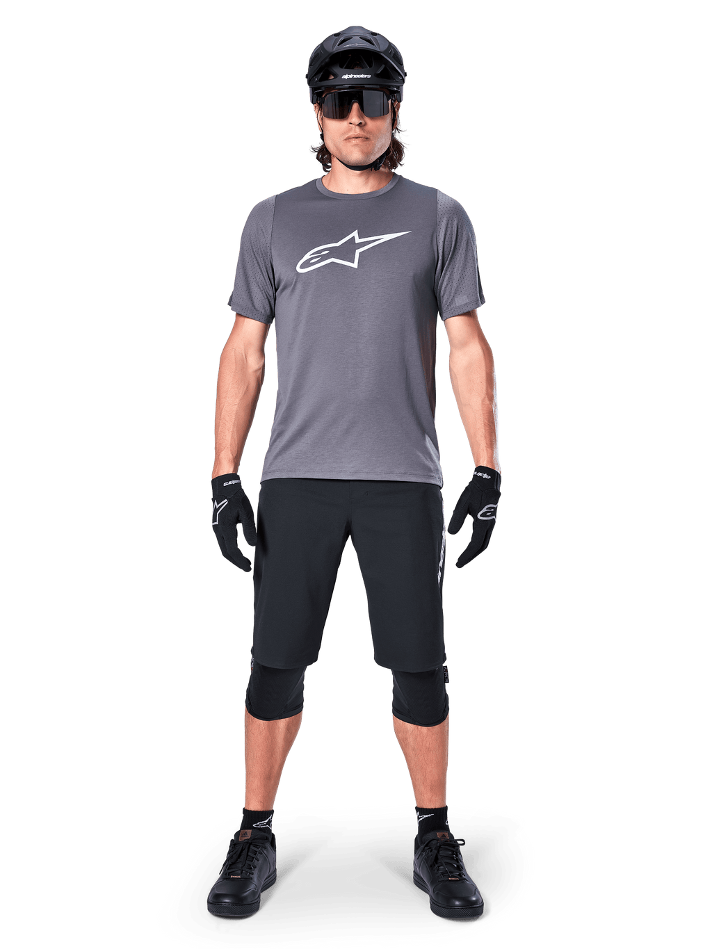 Alpinestars A-Dura Dri Astar Jersey, Short Sleeve Mountain Bike Jersey, Dark Gray, featuring a white Astars logo on the chest, worn with black cycling shorts, knee pads, helmet, and gloves, technical MTB apparel