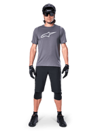 Alpinestars A-Dura Dri Astar Jersey, Short Sleeve Mountain Bike Jersey, Dark Gray, featuring a white Astars logo on the chest, worn with black cycling shorts, knee pads, helmet, and gloves, technical MTB apparel