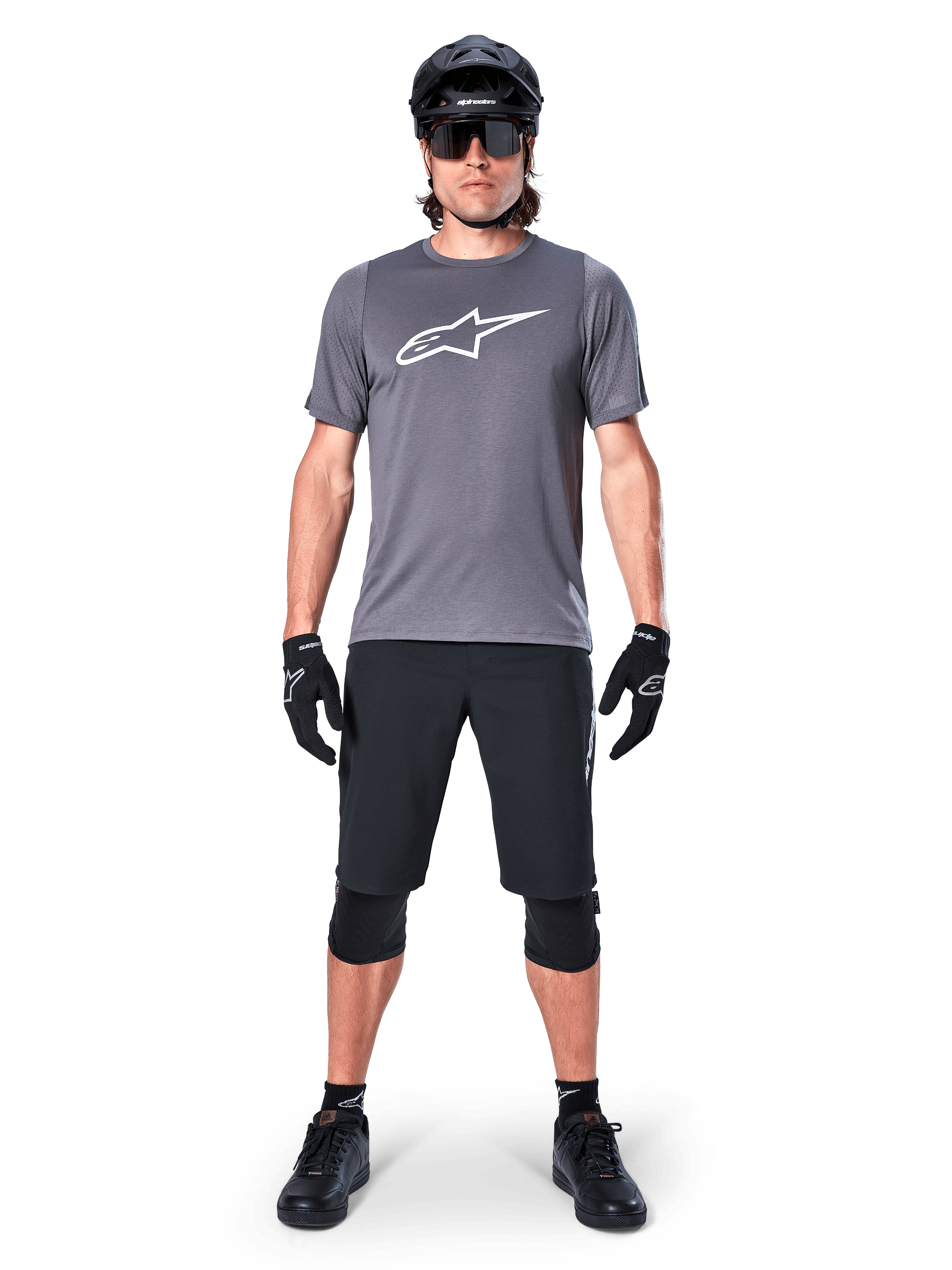 Alpinestars A-Dura Dri Astar Jersey, Short Sleeve Mountain Bike Jersey, Dark Gray, featuring a white Astars logo on the chest, worn with black cycling shorts, knee pads, helmet, and gloves, technical MTB apparel
