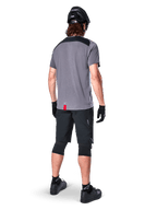 Mountain bike rider seen from behind wearing Alpinestars A-Dura Dri Astar Jersey, Short Sleeve, Dark Gray with black shoulder panels, paired with black MTB shorts, knee pads, and helmet, technical off-road cycling apparel