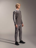 Male model wearing Alpinestars A-Dura Dri Wool Long Sleeve Jersey in Dark Gray, paired with matching gray pants and black shoes, featuring light gray mesh panels on the shoulders and sleeves, technical MTB gear for off-road cycling