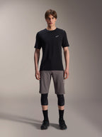 Male model wearing Alpinestars A-Dura Elite Shorts in Dark Gray and A-Dura Dri-Wool Short Sleeve Jersey in Black, paired with black knee guards and cycling shoes, technical mountain bike apparel for off-road performance.