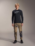 Alpinestars A-Dura Camo Pant, MTB Cycling Pants, Brown and Green Camouflage, worn with a black long-sleeve jersey and black shoes, sporty mountain bike style with durable stretch fabric