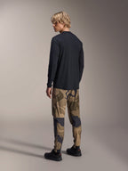 Alpinestars A-Dura Camo Pant, MTB Pants, Brown Camouflage, worn with a black long-sleeve jersey and black sneakers, rear view showing tapered legs and elasticated cuffs, performance apparel for off-road cycling