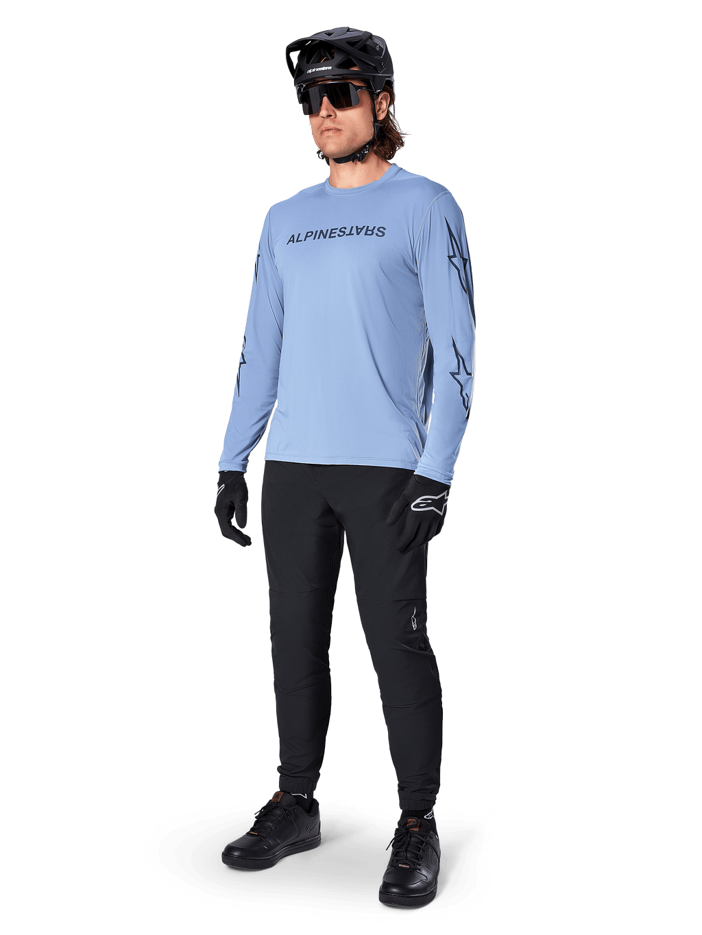 Alpinestars A-Dura Switch Long Sleeve Jersey, Infinity Blue, worn by a rider with black MTB pants, black helmet, and gloves, featuring a chest wordmark logo and star graphics on the sleeves, lightweight cycling gear for trail riding