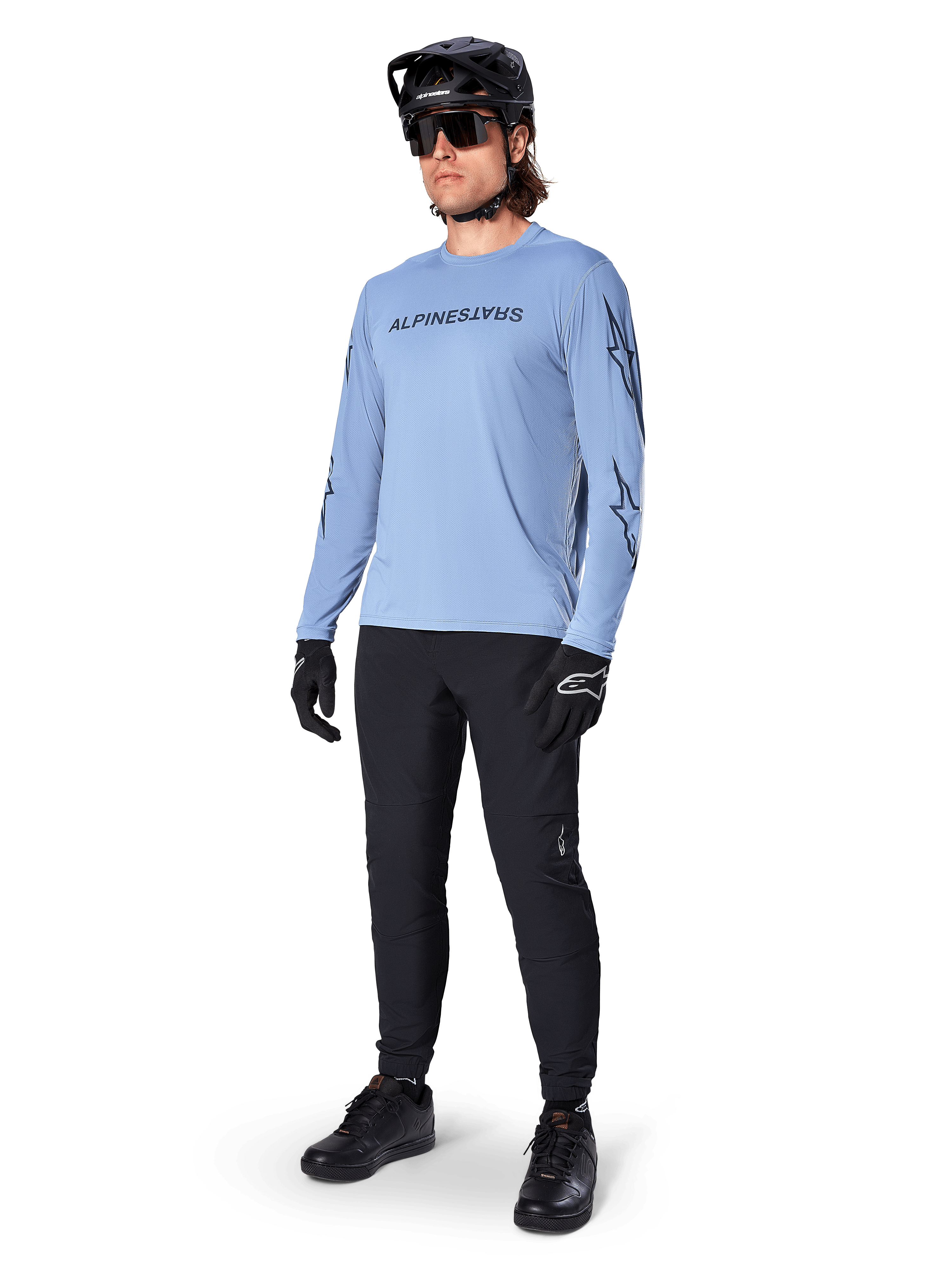 Alpinestars A-Dura Switch Long Sleeve Jersey, Infinity Blue, worn by a rider with black MTB pants, black helmet, and gloves, featuring a chest wordmark logo and star graphics on the sleeves, lightweight cycling gear for trail riding