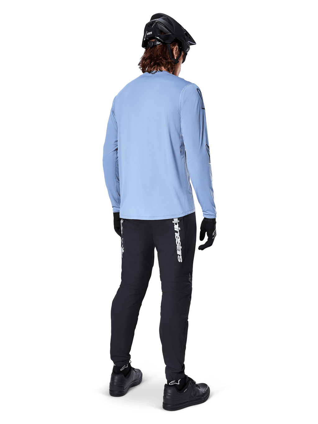 Mountain bike rider from behind wearing Alpinestars A-Dura Switch Long Sleeve Jersey in Infinity Blue, paired with black MTB pants, black helmet, and black shoes, casual trail gear for off-road cycling