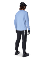 Mountain bike rider from behind wearing Alpinestars A-Dura Switch Long Sleeve Jersey in Infinity Blue, paired with black MTB pants, black helmet, and black shoes, casual trail gear for off-road cycling