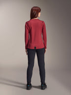 Woman wearing Alpinestars Stella A-Dura Thermal Jersey, Burgundy, rear view, long-sleeve insulated cycling jersey with an extended drop tail, paired with black pants and black riding shoes, outdoor mountain bike apparel.