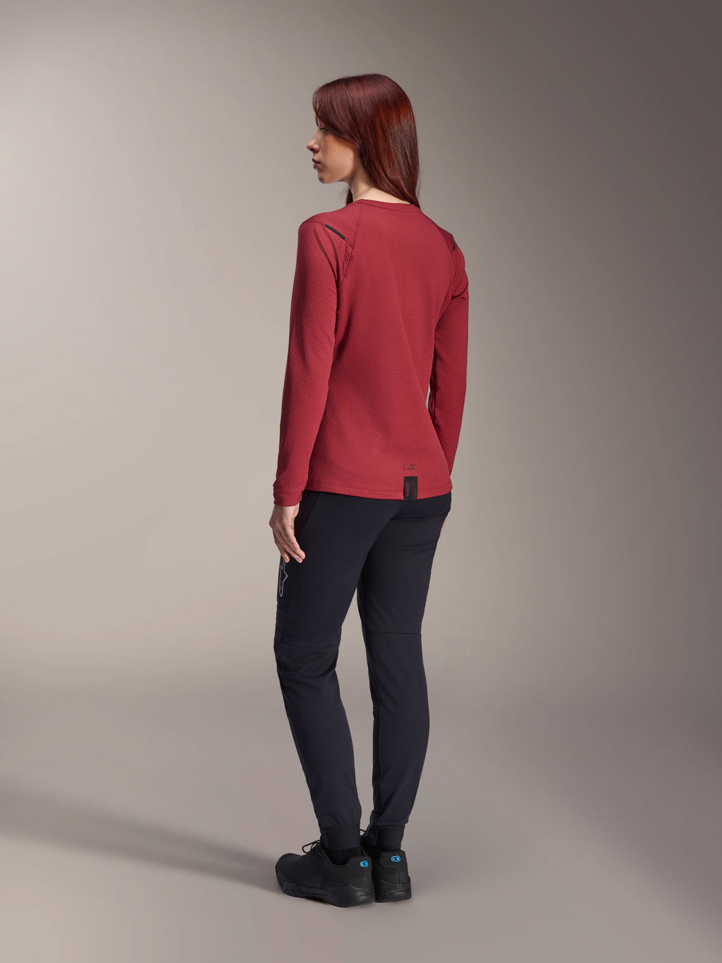 Alpinestars Stella A-Dura Thermal Jersey, Women's long-sleeve mountain bike jersey, Burgundy, back view highlighting the extended drop tail and thermal fabric texture, worn with black MTB pants and black footwear