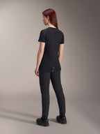 Woman model with red hair wearing the Alpinestars Stella A-Dura Dri Switch Short Sleeve Jersey in Black, rear view, paired with black mountain bike pants and shoes, showing the technical fit and longer drop tail for cycling coverage.