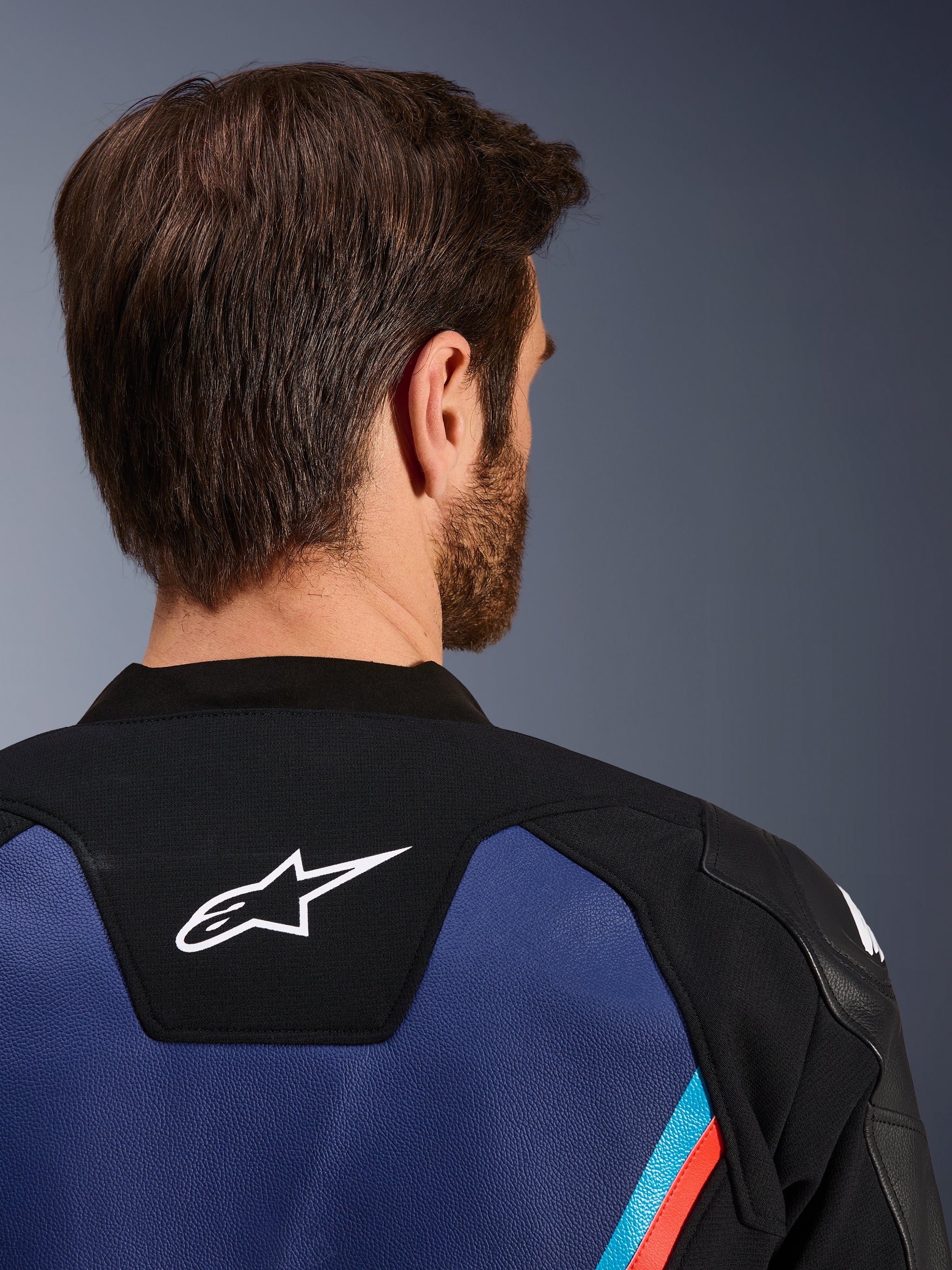 Alpinestars GP Force V2 Leather Jacket, close-up back view of the neck and upper shoulders, white Astars logo on black panel, blue leather construction with fluorescent red and light blue accents, sport riding gear