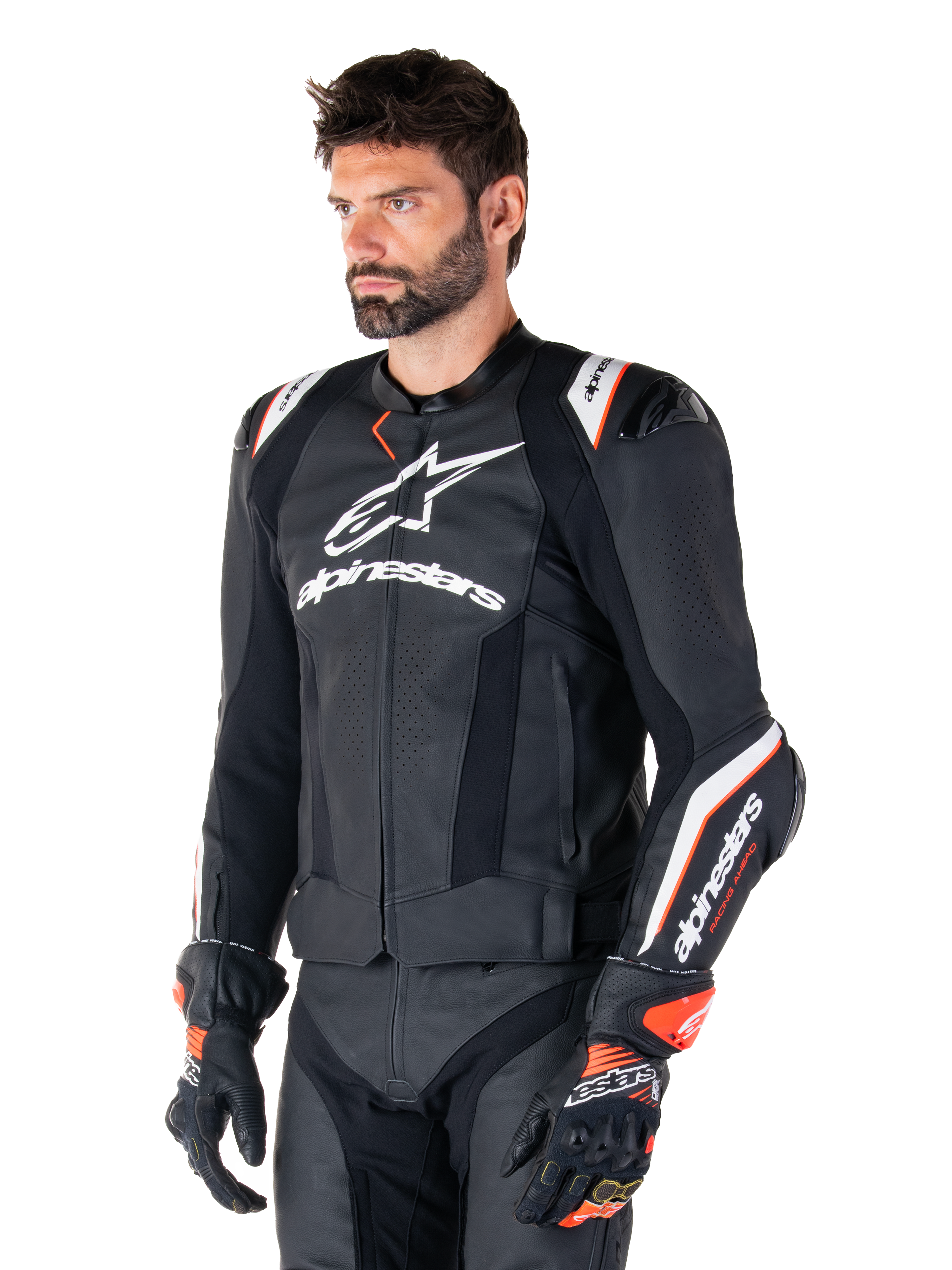 Male model wearing the Alpinestars Missile V3 Ignition Leather Jacket, Black with White and Orange accents, featuring prominent white logos, perforated leather sections, and protective shoulder armor, styled with racing gloves for a sport-racing look.