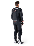 Rear view of a rider wearing the Alpinestars Missile V3 Ignition Leather Jacket in Black, featuring a slim sport Aero-hump with white and red accents, Alpinestars branding on the lower back, paired with matching black leather pants and black and white racing boots, professional sport riding outfit