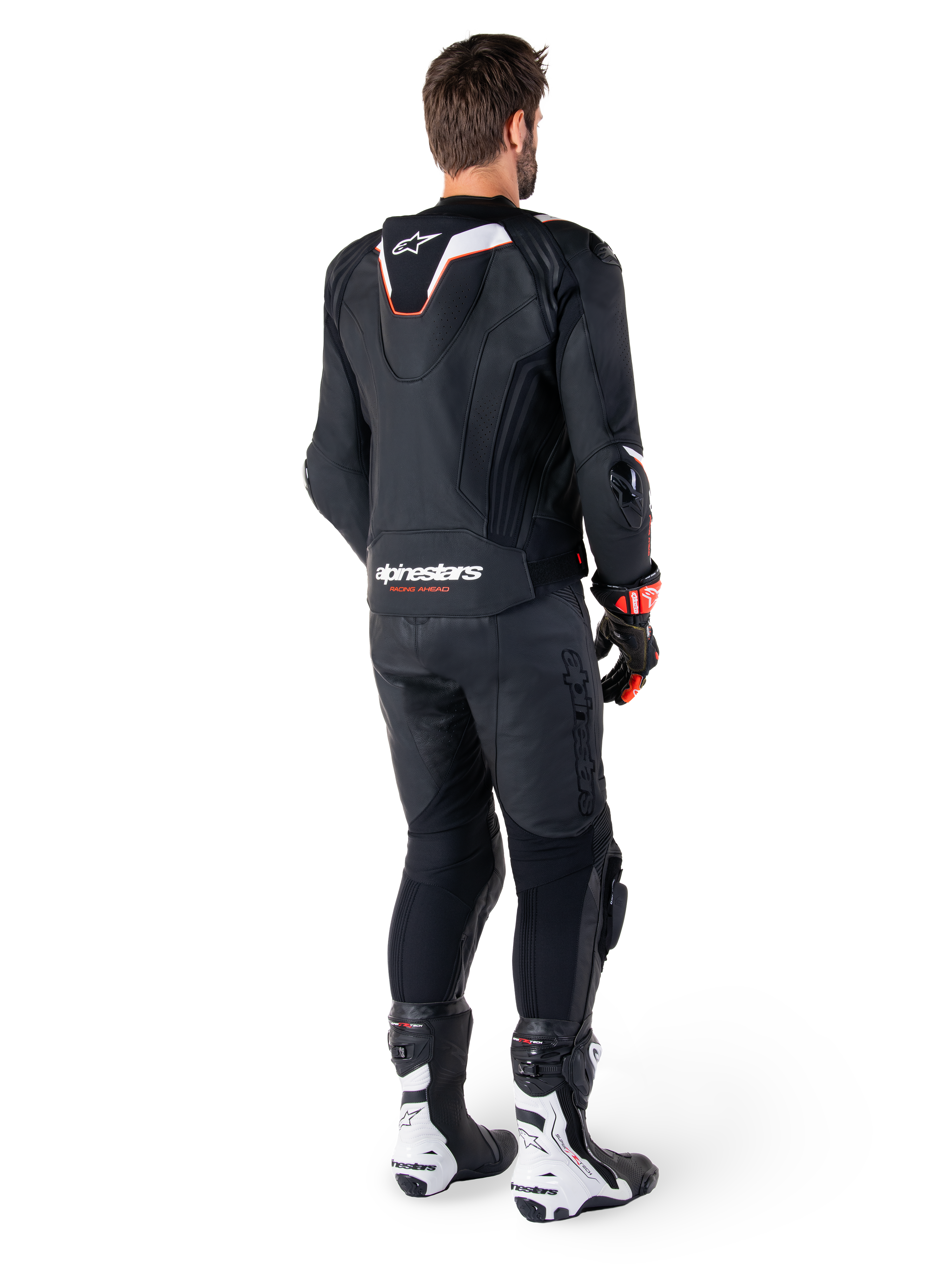 Rear view of a rider wearing the Alpinestars Missile V3 Ignition Leather Jacket in Black, featuring a slim sport Aero-hump with white and red accents, Alpinestars branding on the lower back, paired with matching black leather pants and black and white racing boots, professional sport riding outfit