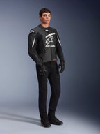 Alpinestars GP Plus V4 Leather Jacket, Sport Motorcycle Jacket, Black and White, worn by a male model with black riding pants and gloves, featuring a large white ASTARS logo on the chest and external DFS shoulder sliders, professional racing-derived design