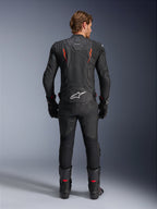 Alpinestars Dusk Airflow Leather Jacket, Black and Red Fluo, rear view showing extensive perforations and large white logo on the lower back, worn with matching leather racing gear including pants, boots, and gloves