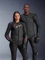 Alpinestars Stella Dusk Leather Jacket, Black Diva Pink White, worn by a female model alongside a male model in matching black leather gear, featuring pink and white accents, white star logo on chest, and black riding gloves