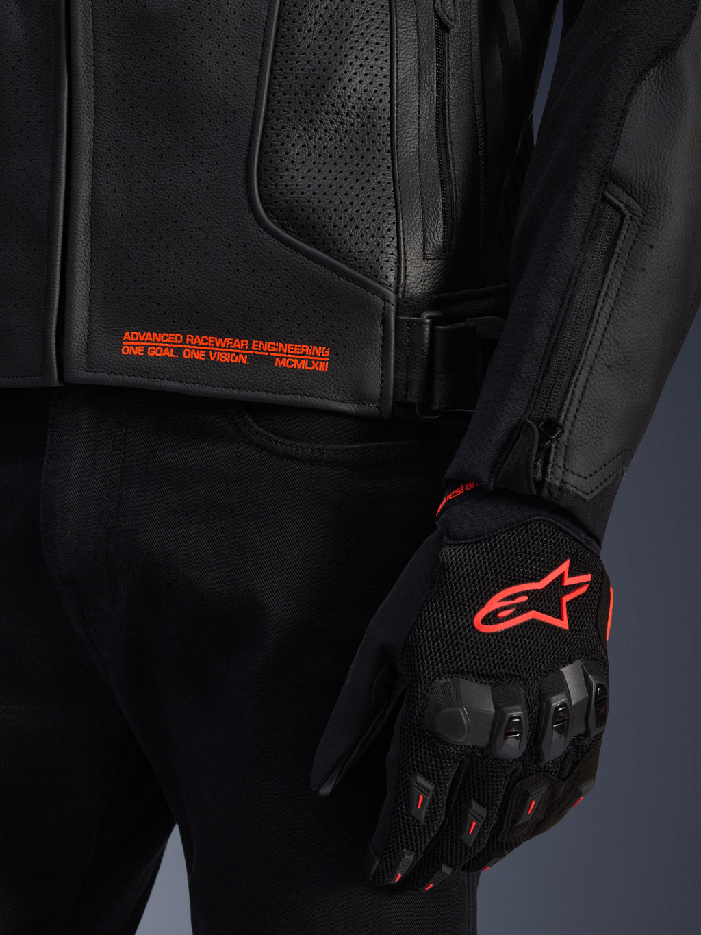 Alpinestars GP Plus R V4 Airflow Leather Jacket, close-up of black perforated leather with orange graphic text, paired with a black and orange motorcycle glove featuring the Astars logo