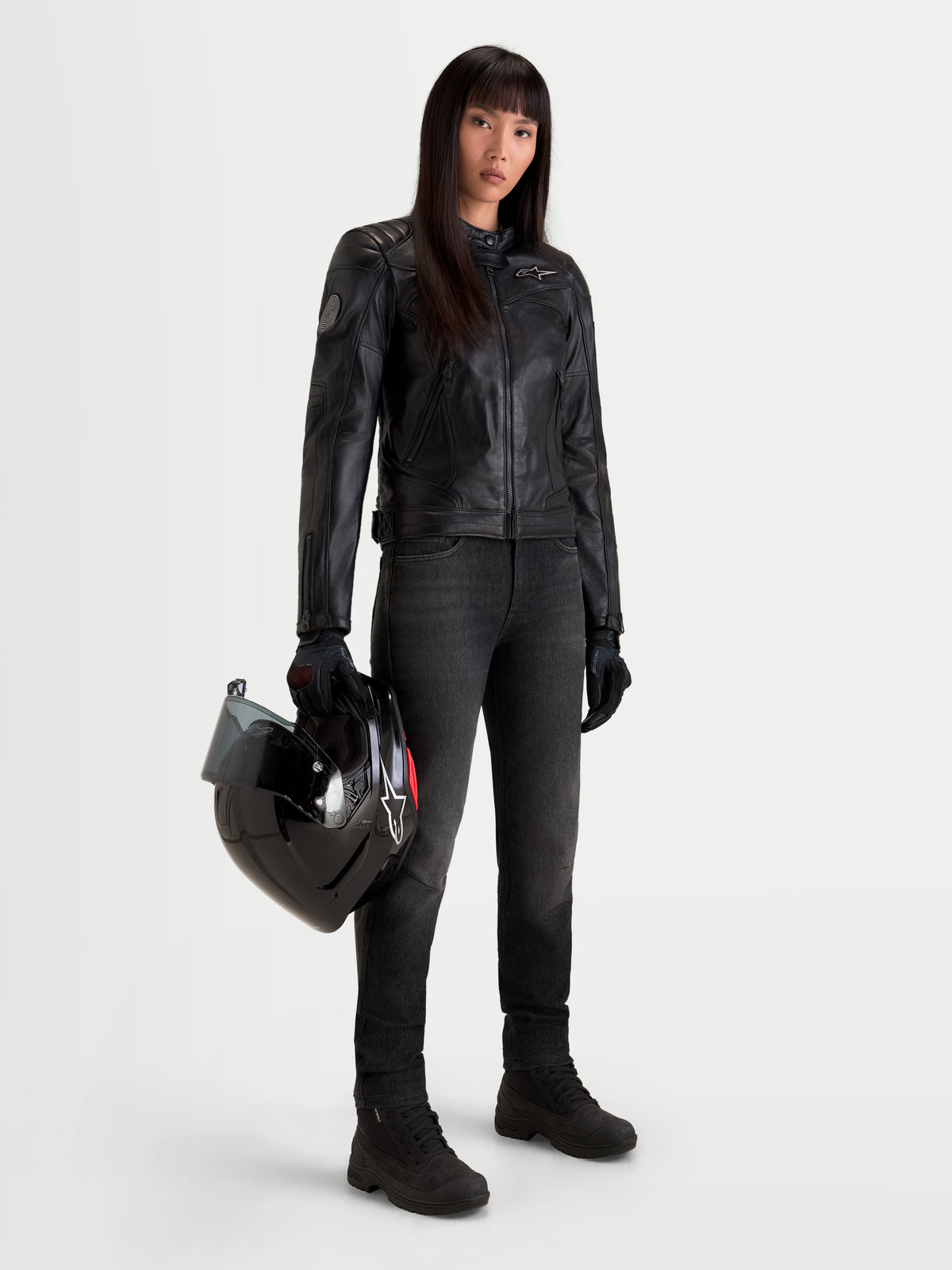 Alpinestars Revea Women Leather Jacket, women's urban contemporary motorcycle leather jacket in black, full-grain bovine leather construction worn by a female model holding a helmet, AA certified protection.
