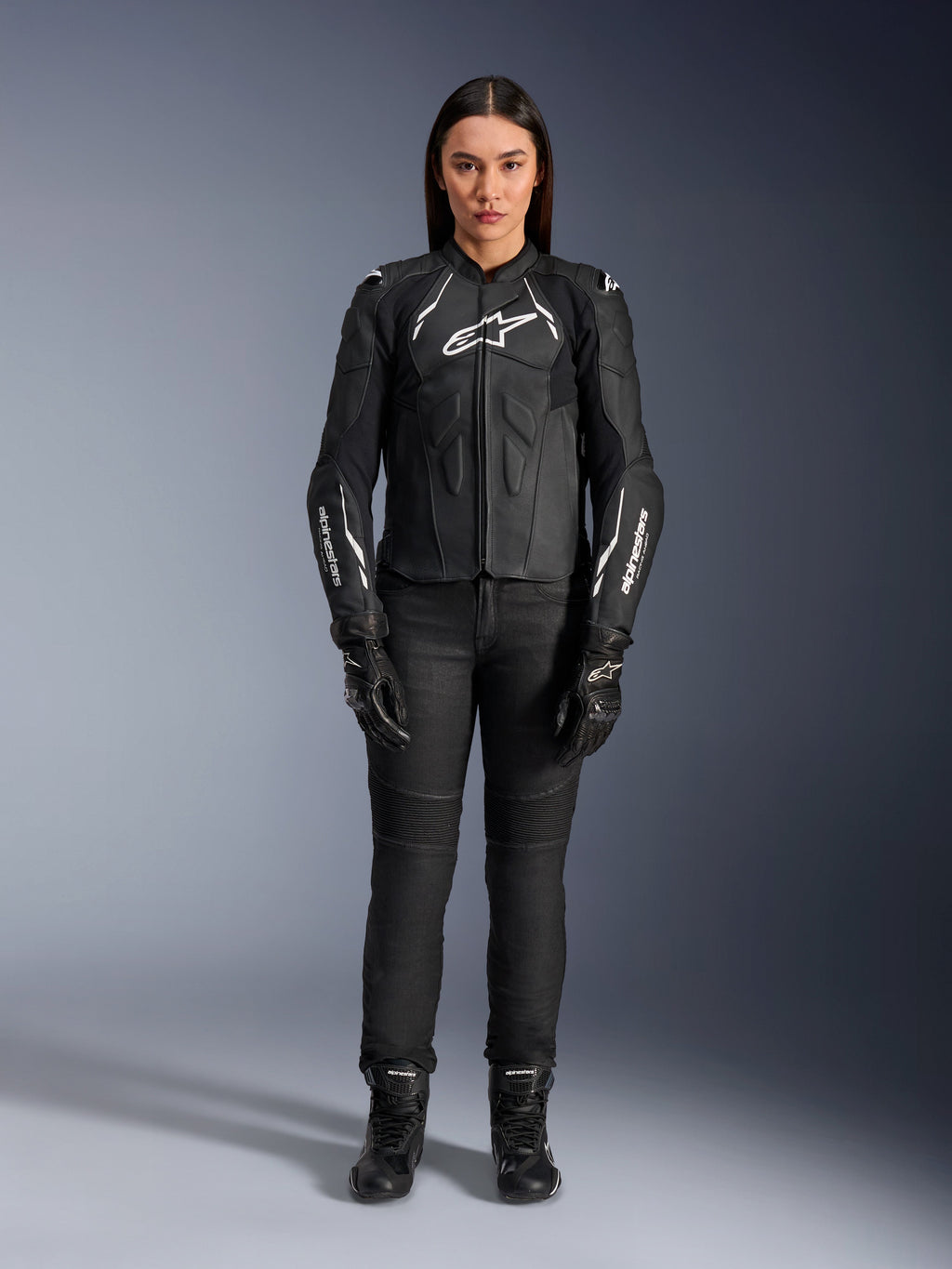 Alpinestars Woman Stella Dusk Leather Jacket, Black and White, worn by a model with matching black pants and boots, front view, featuring white Alpinestars logos on the chest and sleeves, premium bovine leather protective gear for women