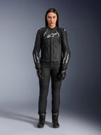 Alpinestars Woman Stella Dusk Leather Jacket, Black and White, worn by a model with matching black pants and boots, front view, featuring white Alpinestars logos on the chest and sleeves, premium bovine leather protective gear for women