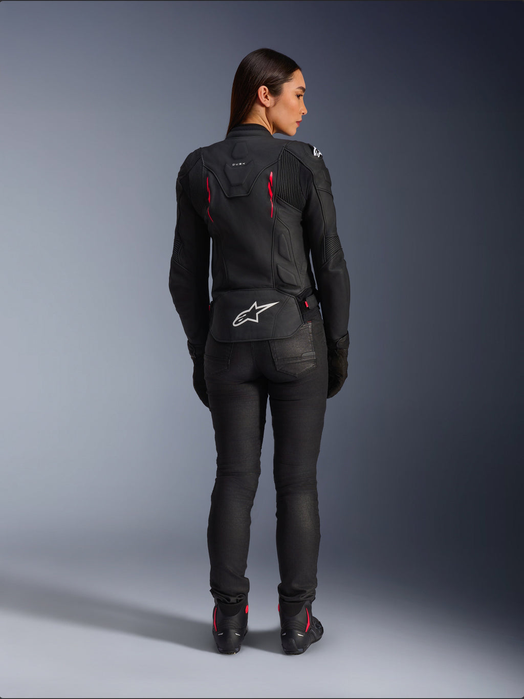 Alpinestars Stella Dusk Leather Jacket, rear view, black leather with Diva Pink and White accents, features white Alpinestars logo on lower back and pink vent details, worn with black riding pants and boots, premium sport motorcycle gear for women