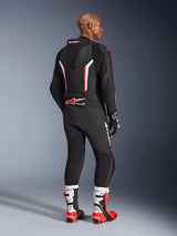 Rider wearing the GP Force V2 Leather Suit 1-Piece, Black with White and Red Fluo accents, seen from the back showing the aerodynamic speed hump and Alpinestars branding, paired with matching racing gloves and white and red performance boots, professional motorcycle racing gear