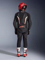 Rider viewed from behind wearing the Alpinestars GP Force V2 Leather Suit 1-Piece in Black White Red Fluo, featuring an aerodynamic speed hump and Tech-Air Ready branding, coordinated with a red racing helmet and white and red boots, professional track gear design.