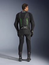 Rear view of the Alpinestars GP Force V2 1-Piece Leather Suit in Black and Green, featuring an aerodynamic speed hump, perforated panels, and Tech-Air Ready branding on the lower back, worn with black racing gloves and boots.