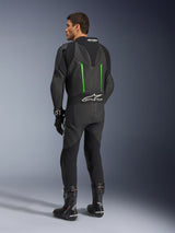 Alpinestars GP Force V2 Leather Suit, 1-Piece Motorcycle Suit, Black with Green accents, back view showing the aerodynamic speed hump and white logo on the accordion stretch panel, paired with black racing boots and gloves.