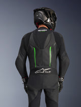 Rear view of a rider wearing the Alpinestars GP Force V2 Leather Suit in Black Green, featuring an aerodynamic speed hump, Tech-Air Ready branding on the lower back accordion panel, and perforated leather construction, paired with a black carbon fiber racing helmet.