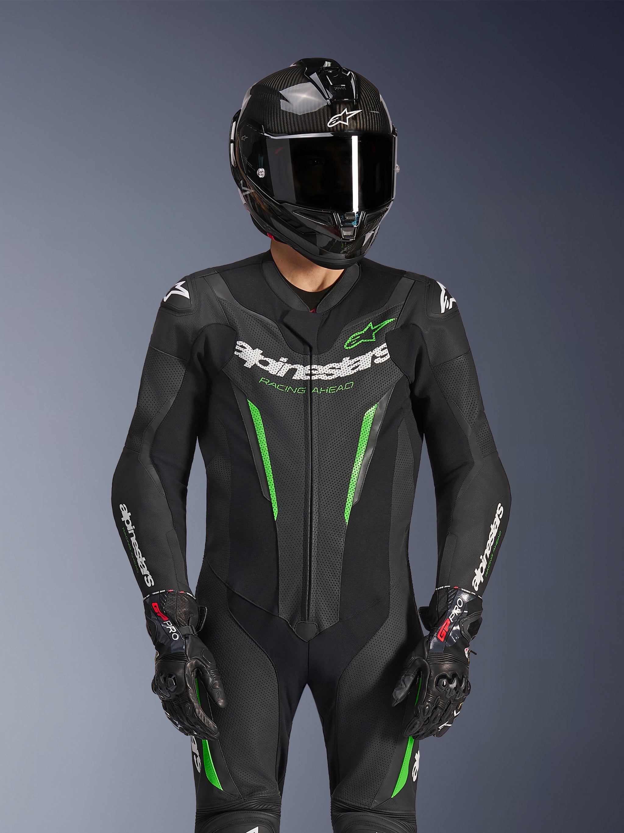 Alpinestars GP Force V2 Leather Suit - 1Piece, Black and Green, motorcycle racing suit worn with a carbon fiber helmet and GP Pro gloves, featuring lime green accents and Alpinestars 'Racing Ahead' branding, engineered for track performance.