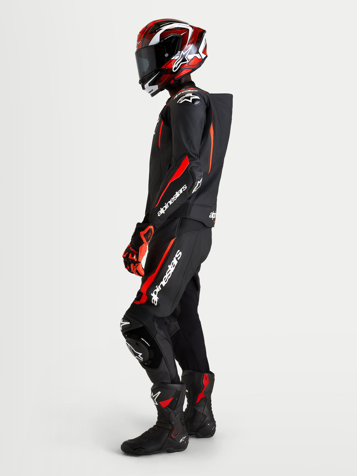 Alpinestars Missile V3 Leather Suit 2 Piece, Black and Red Fluo, men's two-piece motorcycle racing leather suit worn by a rider with matching helmet, featuring AAA abrasion resistance, aerodynamic speed hump, and protective armor