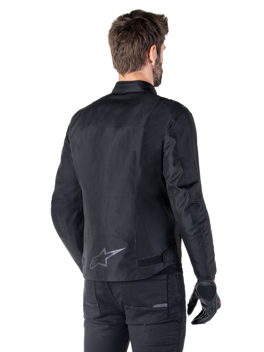 Alpinestars T-SPS V2 Waterproof Jacket, Black, rear view on a male model, featuring a reflective star logo on the lower back, extended back profile, and waist adjustment straps, paired with black riding pants and gloves