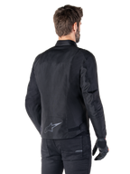 Alpinestars T-SPS V2 Waterproof Jacket, Black, rear view on a male model, featuring a reflective star logo on the lower back, extended back profile, and waist adjustment straps, paired with black riding pants and gloves