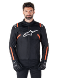 Alpinestars T-SPS V2 Waterproof Jacket, Black White and Red Fluo, worn by a male model with black riding gloves, featuring a large white Alpinestars logo on the chest and vibrant orange accents on the shoulders and sleeves.
