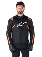 Alpinestars T-SPS V2 Waterproof Jacket, Black White and Red Fluo, worn by a male model with black riding gloves, featuring a large white Alpinestars logo on the chest and vibrant orange accents on the shoulders and sleeves.