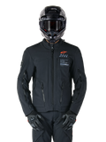 Alpinestars AMT-8 Stretch Drystar® XF Jacket, Black Motorcycle Jacket, featuring orange Alpinestars logo and grey AMT branding, high collar with front zipper and vents, worn with black helmet and gloves, protective adventure touring gear
