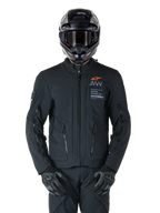 Alpinestars AMT-8 Stretch Drystar® XF Jacket, Black Motorcycle Jacket, featuring orange Alpinestars logo and grey AMT branding, high collar with front zipper and vents, worn with black helmet and gloves, protective adventure touring gear