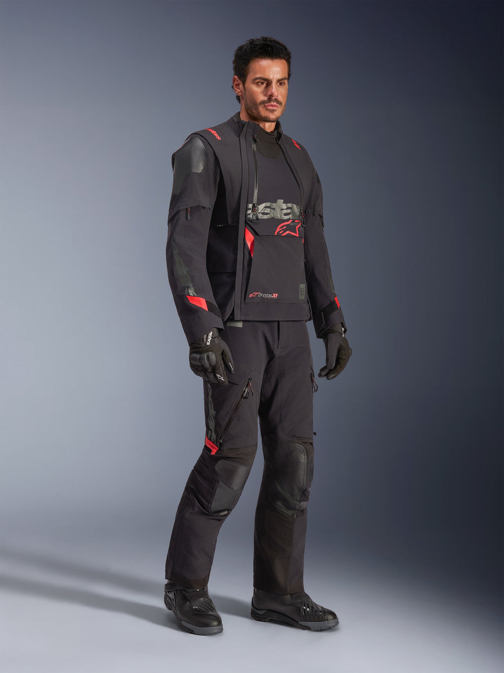 Male rider wearing the Alpinestars Halo Pro Drystar® XF Laminated Jacket in Black Dark Shadow, complete adventure riding gear with matching pants, gloves, and boots, featuring modular asymmetrical front panels and red branding accents.