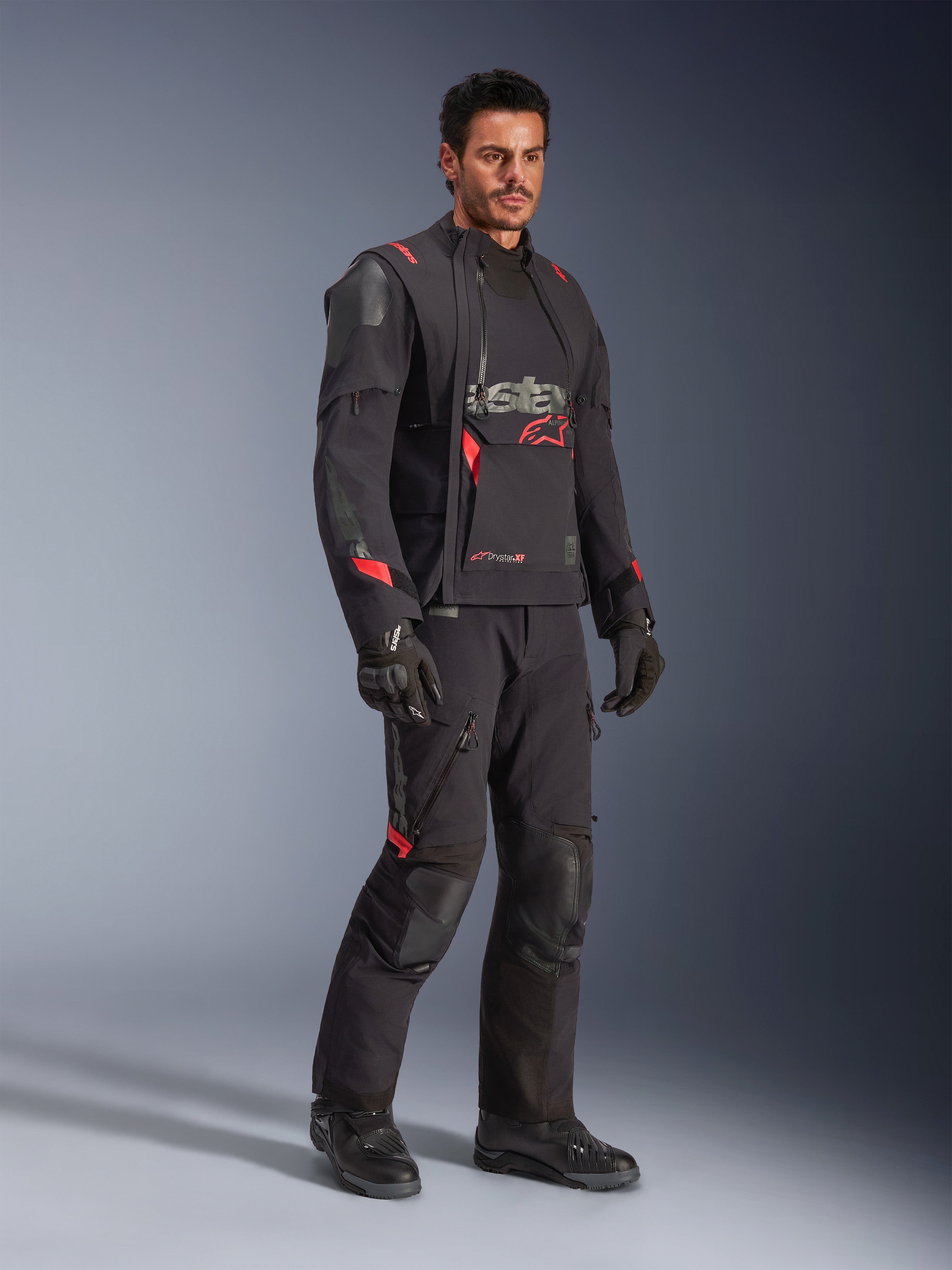 Male rider wearing the Alpinestars Halo Pro Drystar® XF Laminated Jacket in Black Dark Shadow, complete adventure riding gear with matching pants, gloves, and boots, featuring modular asymmetrical front panels and red branding accents.