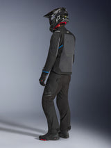 Motorcycle rider wearing the Alpinestars Cusco Drystar® Jacket in Black and Deep Gray with blue accents, paired with black riding pants, a carbon fiber SM10 helmet, and black gloves, back view showing the large ventilation panel and adventure touring design.
