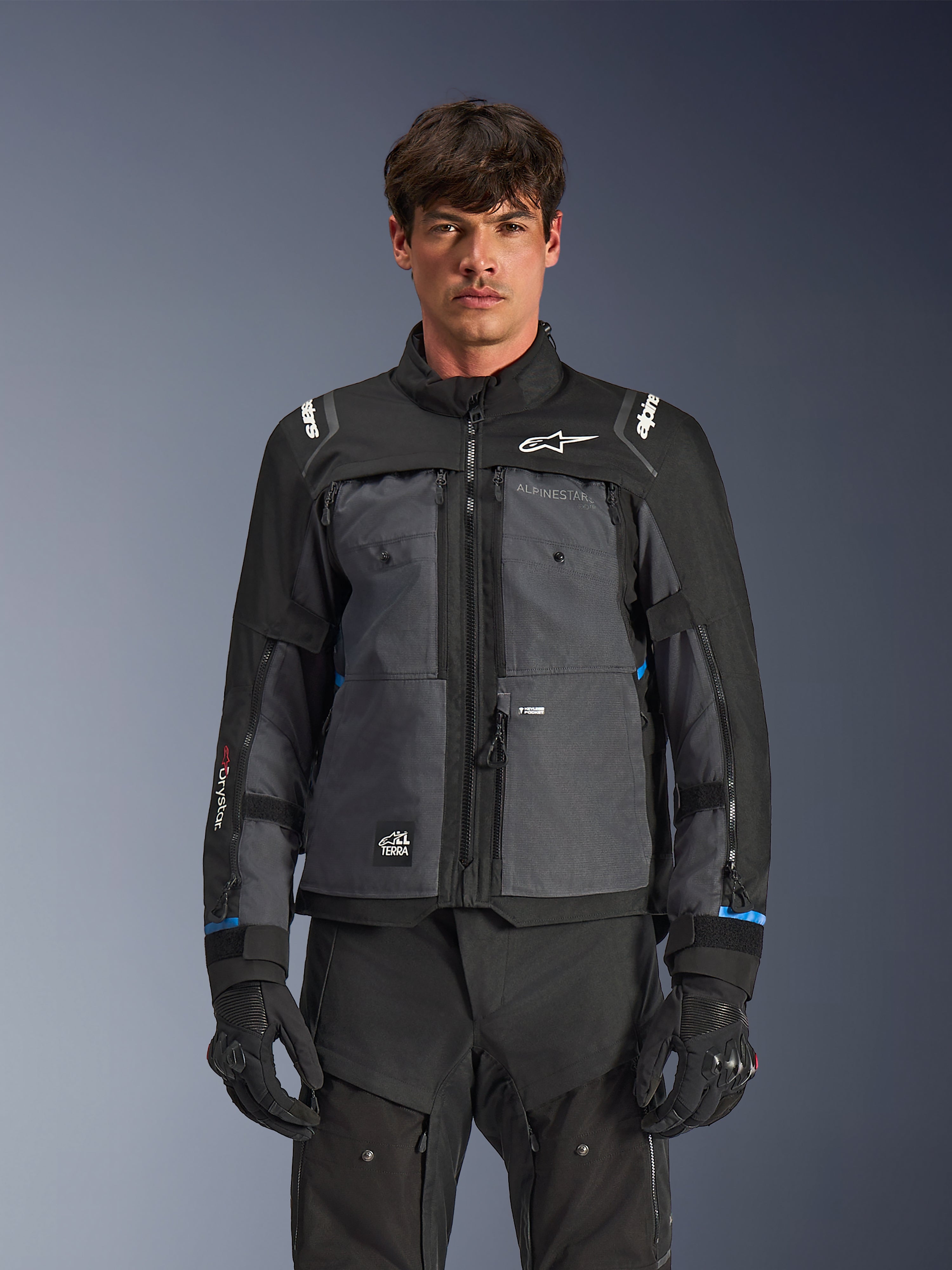 Alpinestars Cusco Drystar® Jacket, Motorcycle Touring Jacket, Black and Deep Gray, front view on model, featuring Alpinestars logos on chest and shoulders, Drystar® sleeve branding, technical multi-pocket design with ventilation zippers, paired with black riding gear